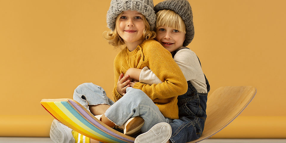Two young children sitting on a curved board with a rainbow base.