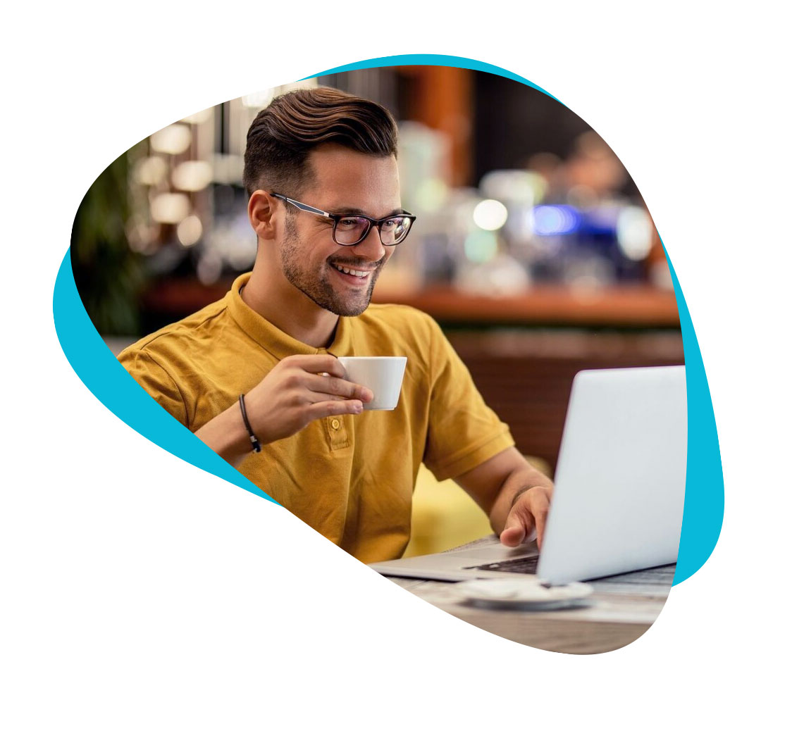 Smiling man holding coffee while working on his laptop.