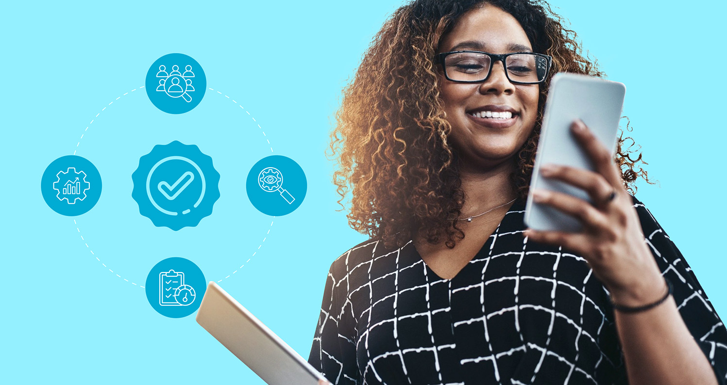 Smiling woman looking at a smartphone while holding a tablet in her other arm.