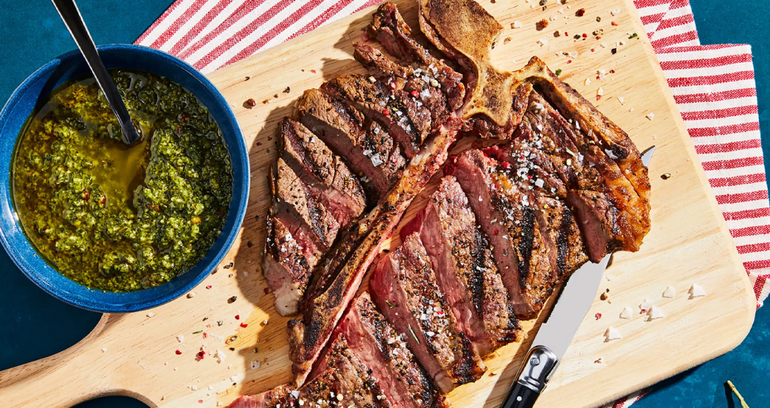 Grilled American-raised T-bone steak with green herb sauce, showcasing premium steak and meat delivery quality.